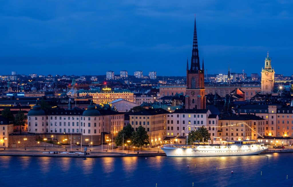 city, cityscape, waterfront, illuminated, ship, architecture, skyline, historic center, church, steeple, water, sea, night, evening, twilight, lights, mirroring, nature, stockholm, sweden, scandinavia